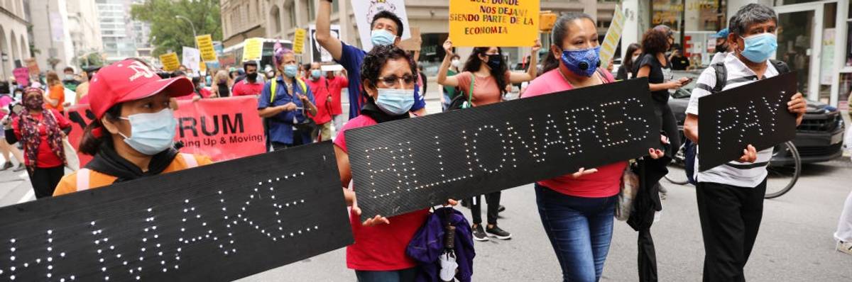 People march down the street with black signs saying, "Make billionaires pay."