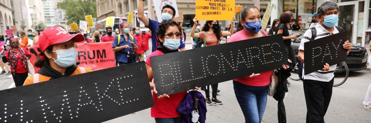 People march down the street with black signs saying, "Make billionaires pay."