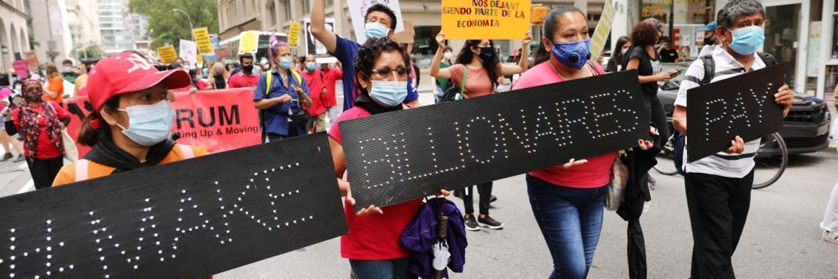 People march down the street with black signs saying, "Make billionaires pay."