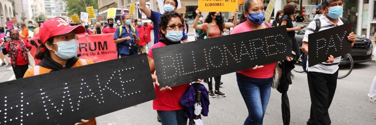 People march down the street with black signs saying, "Make billionaires pay."