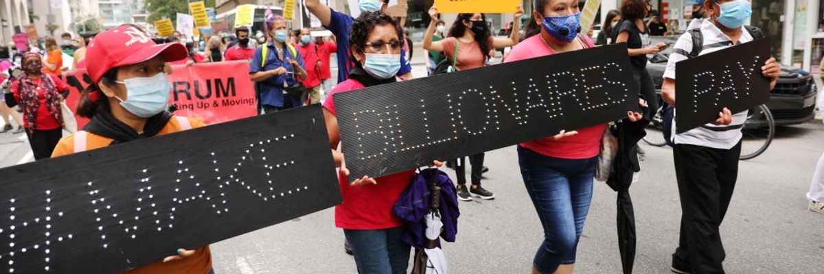 People march down the street with black signs saying, "Make billionaires pay."