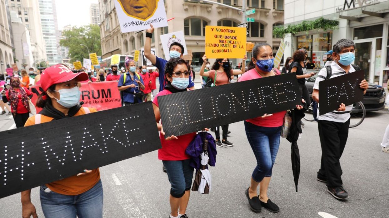 People march down the street with black signs saying, "Make billionaires pay."