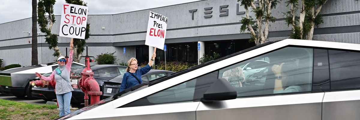 People participate in a "TeslaTakedown" protest against Elon Musk outside of a Tesla with signs that say "Impeach Pres. Elon."