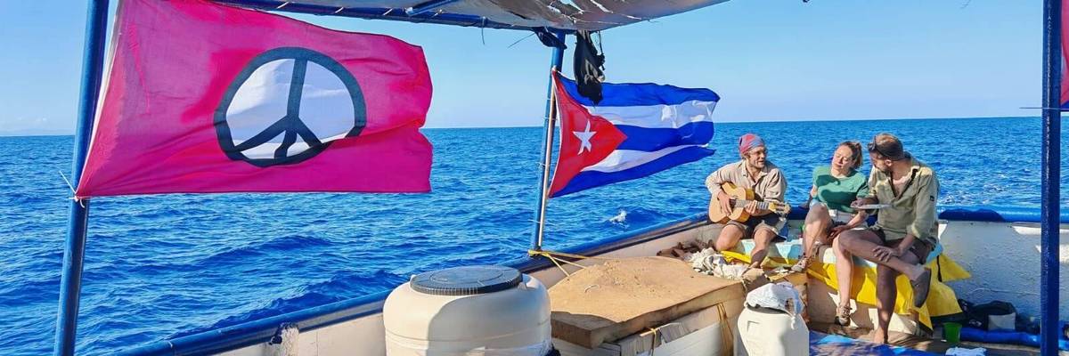 People play music on a boat with a Cuban flag and a peace flag.