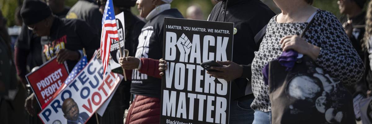 People protest for voting rights; one holds a sign reading "Black voters matter"