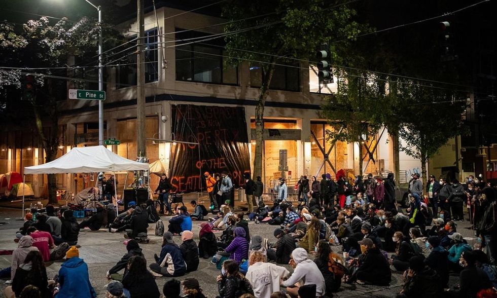 People sit in the street while watching a documentary film screening outside of the Seattle Police Departments East Precinct on June 9, 2020, in Seattle. Protests have continued in many parts of the city including inside City Hall and around the Seattle Police Departments East Precinct, an area that has earned the moniker