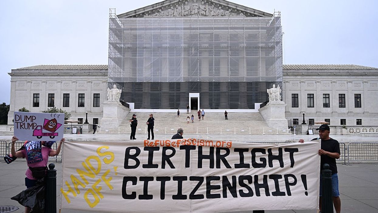 People stand in front of the Supreme Court with a banner reading, "Hands off birthright citizenship."