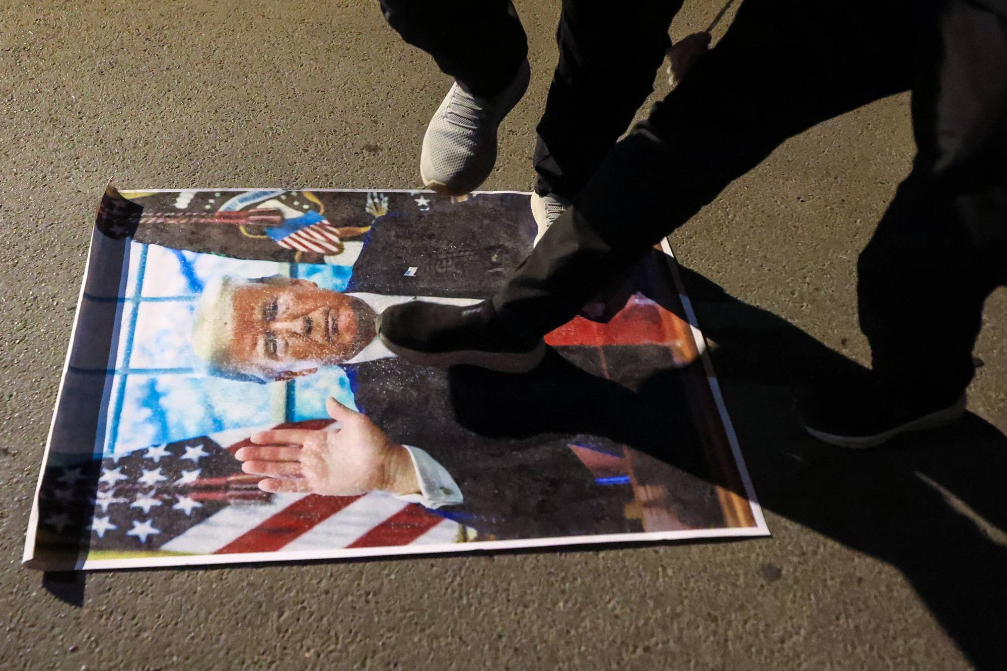 People step on a picture of Trump to protest the Iran War.