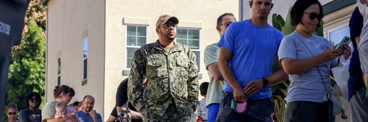 People wait in line to receive free food from volunteers with a food bank
