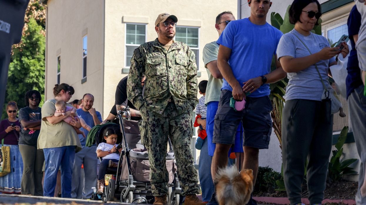 People wait in line to receive free food from volunteers with a food bank