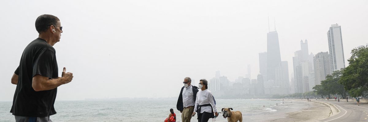 People walk and jog along the shoreline of Lake Michigan with heavy smoke from the Canadian wildfires in the background