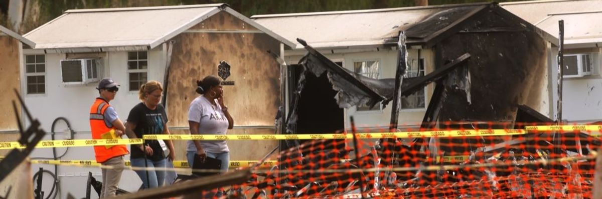 People walk behind caution tape in front of burned tiny homes.