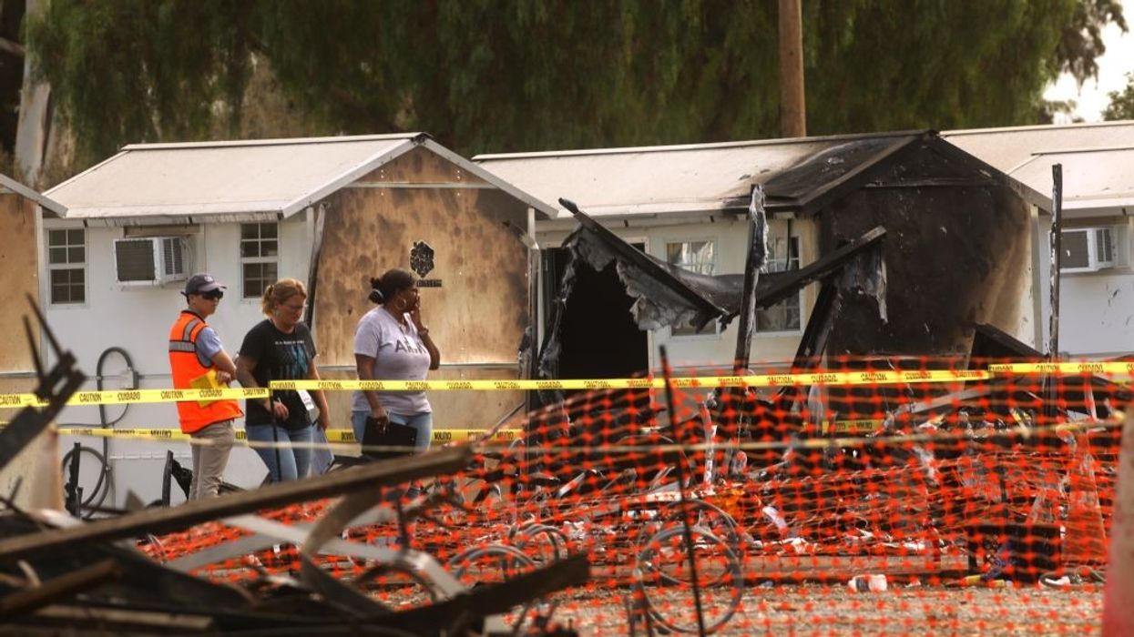 People walk behind caution tape in front of burned tiny homes.