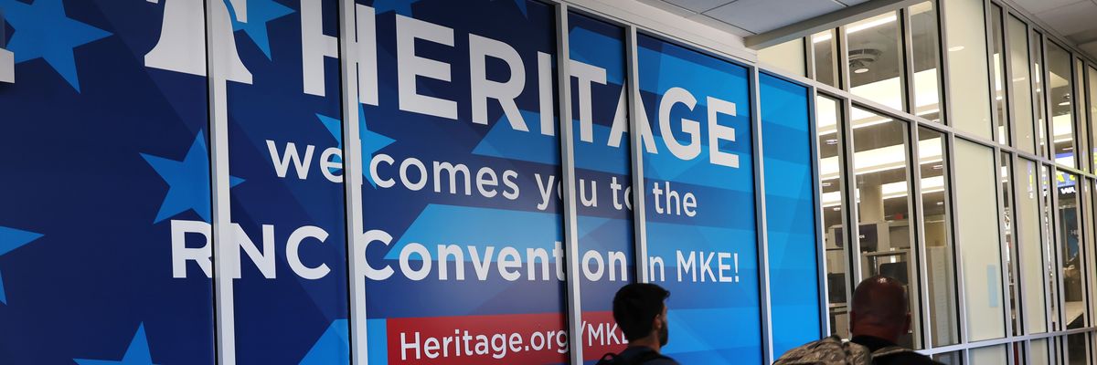 People walk past a Heritage Foundation welcome sign