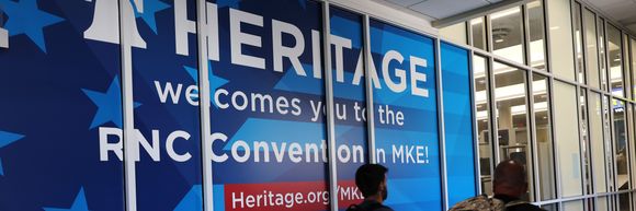 People walk past a Heritage Foundation welcome sign