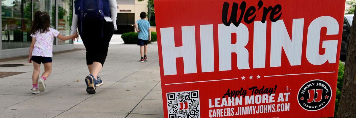 People walk past a "we're hiring" sign