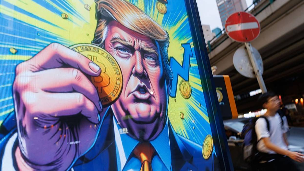 People walk past an advertisement featuring U.S. President Donald Trump with Bitcoin