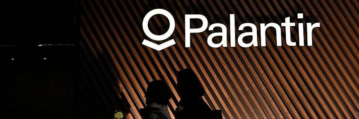 People walk past the Palantir logo.