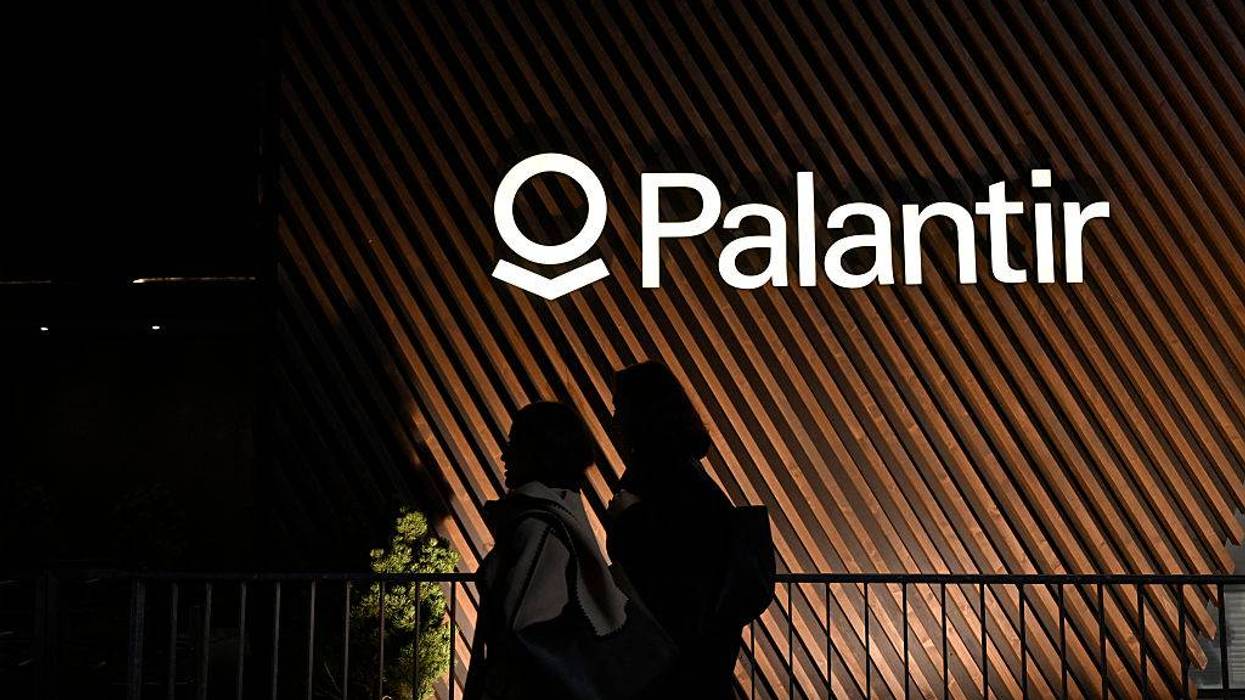 People walk past the Palantir logo.