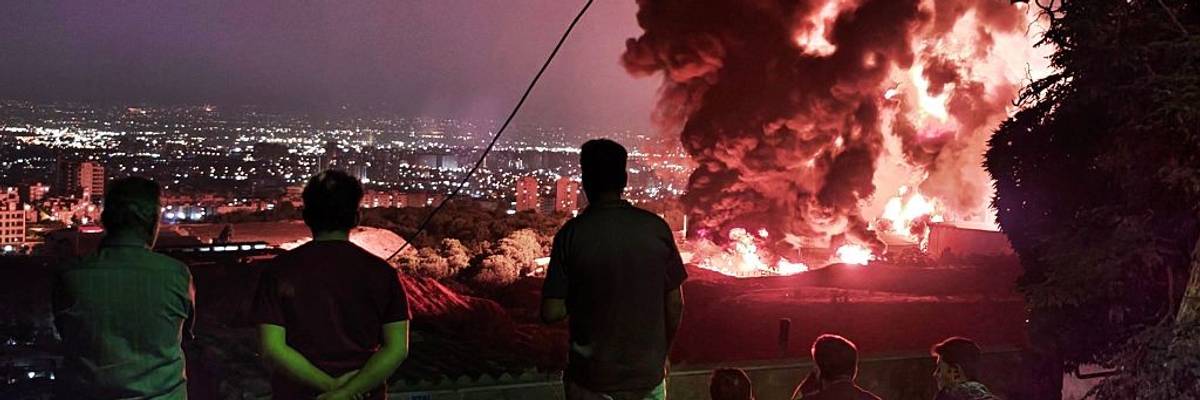 People watch an oil field on fire in Iran after bombing.