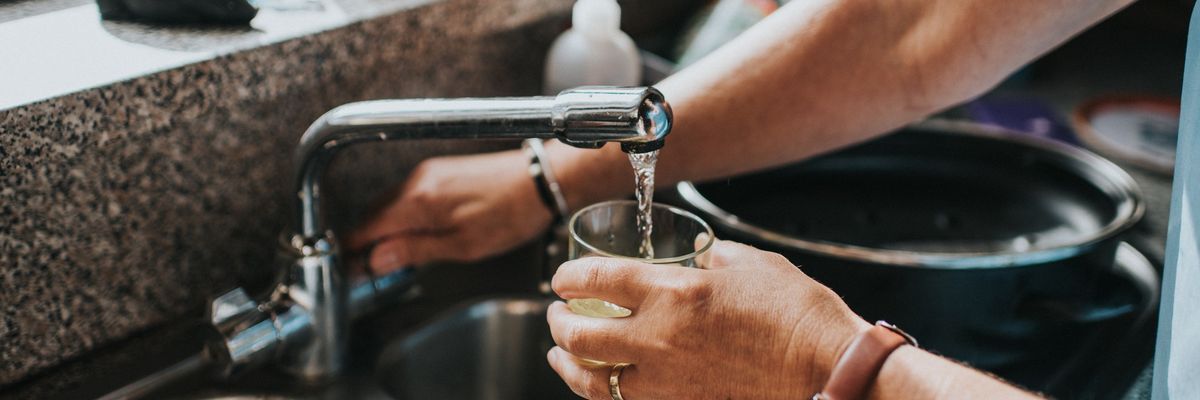 Person at a tap, filling a glass of water.