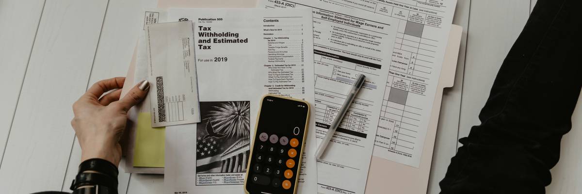 person holding paper near pen and calculator