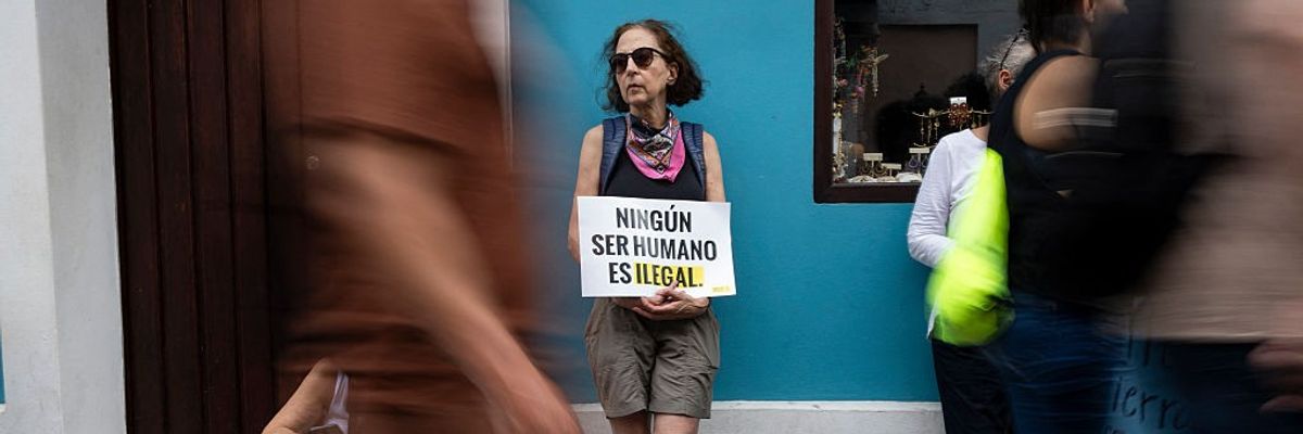 Person holds sign reading, "No human being is illegal," in Spanish.