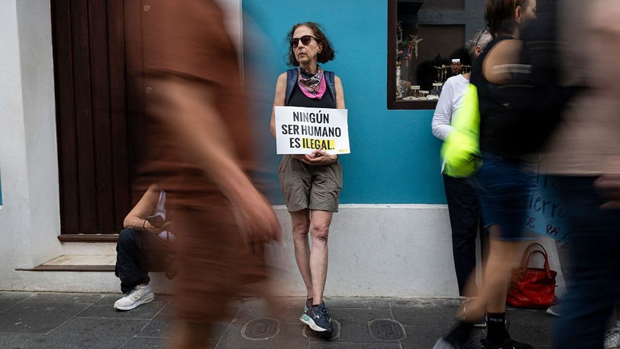 Person holds sign reading, "No human being is illegal," in Spanish.