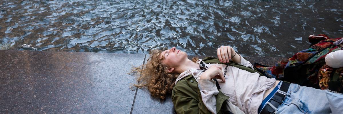 Person rests by fountain during heatwave.