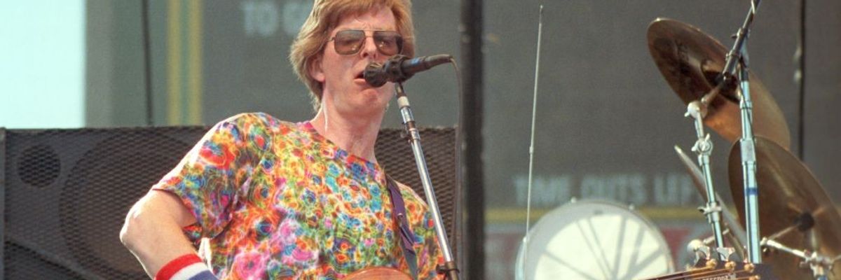 Phil Lesh plays bass wearing a psychedelic t-shirt, sunglasses, and red-white-and-blue wristband