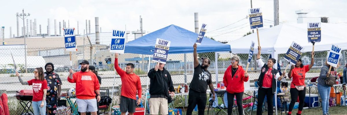 Picketing UAW members hold up signs.