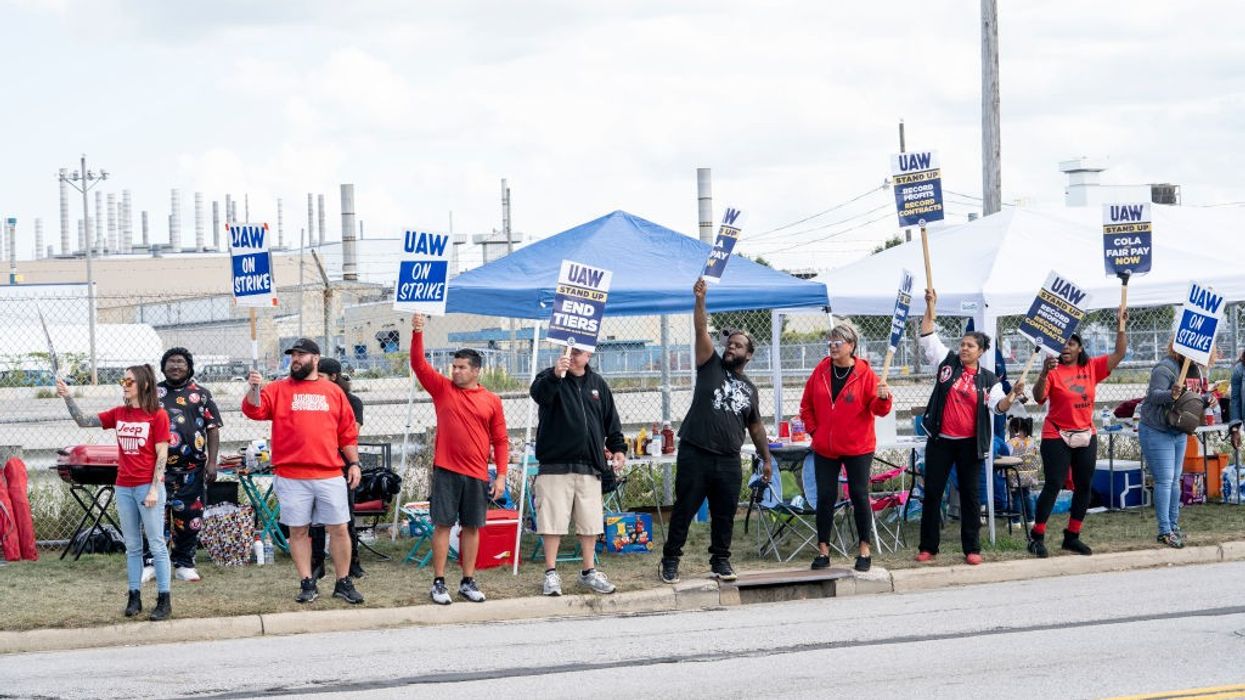 Picketing UAW members hold up signs.