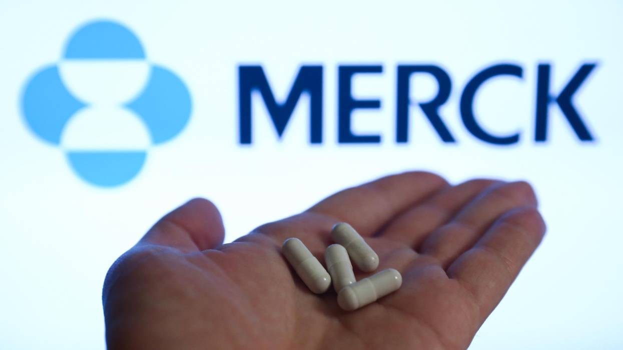 Pills are seen with Merck logo displayed on a screen in the background