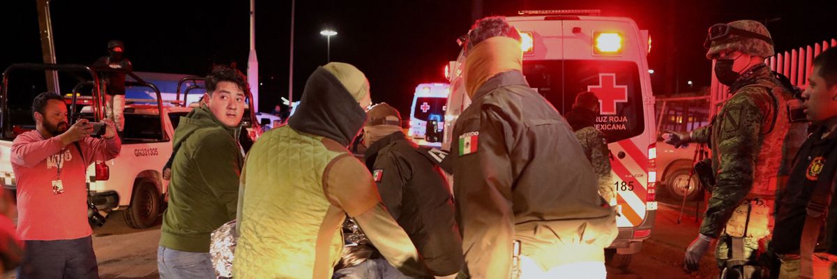 Police officers carry an injured migrant following a fire that killed dozens