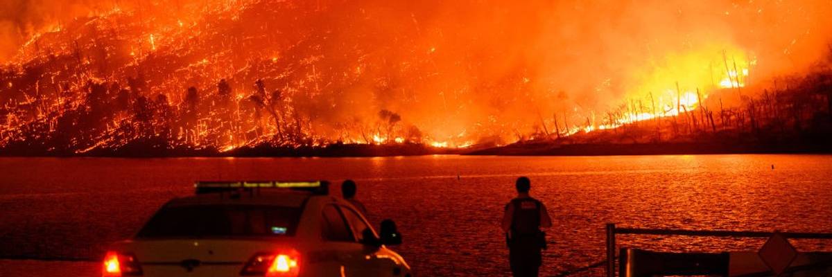 Police watch as a massive wildfire burns over Lake Oroville in California