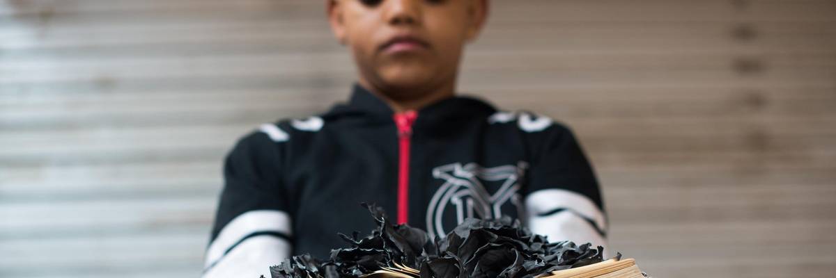 Portrait of a boy holding a burnt book.