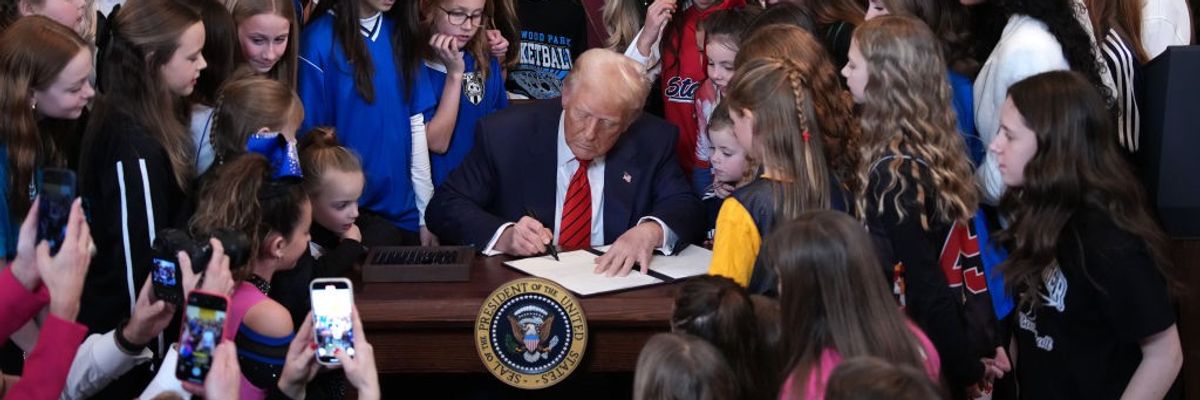 President Donald Trump signs an executive order surrounded by girls