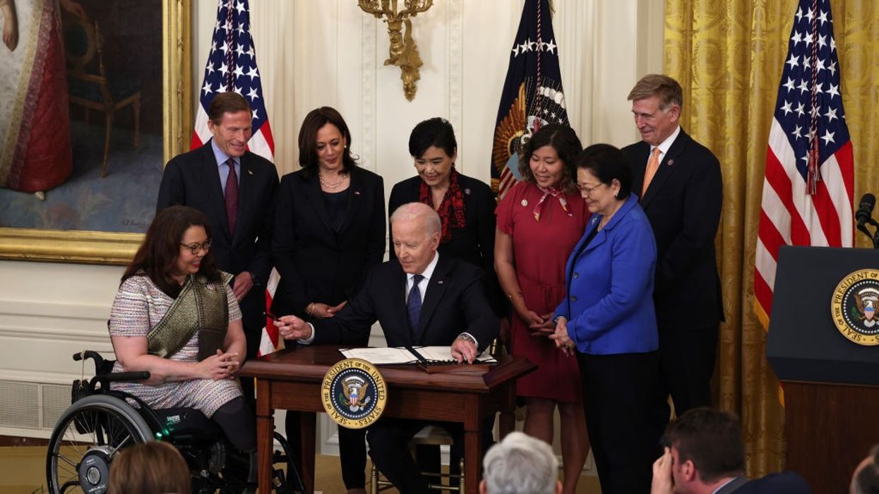 President Joe Biden sits at a desk holding a pen surrounded by members of Congress.