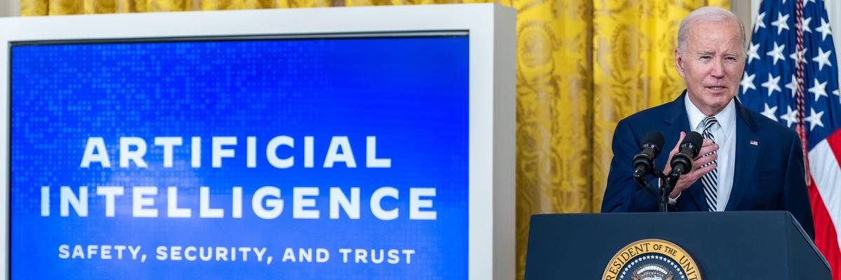 President Joe Biden speaks near a screen reading "Artificial Intelligence: Safety, Security, and Trust"