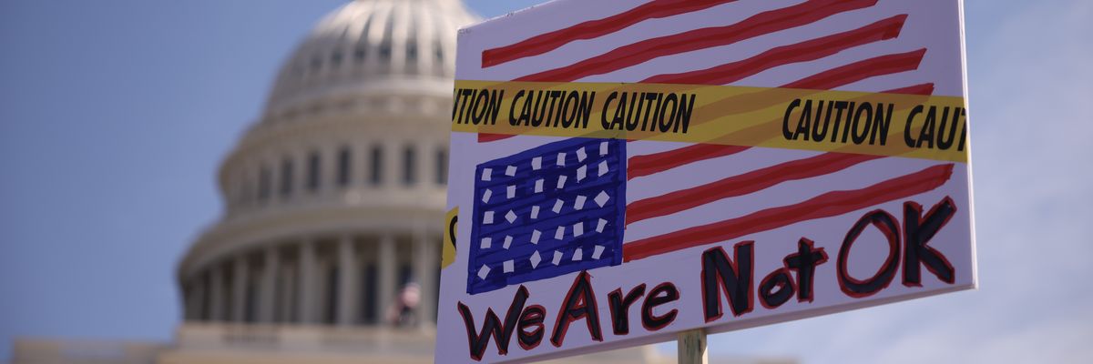 Protest sign with U.S. flag upside down covered with caution tape saying, "We are not OK."