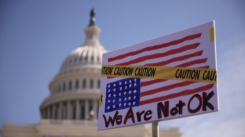 Protest sign with U.S. flag upside down covered with caution tape saying, "We are not OK."
