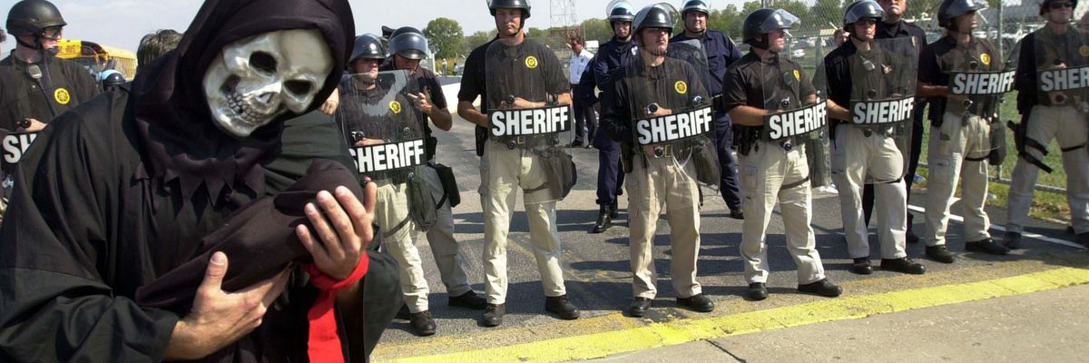 Protester dressed as death holds baby doll near Missouri Boeing plant with police behind them.