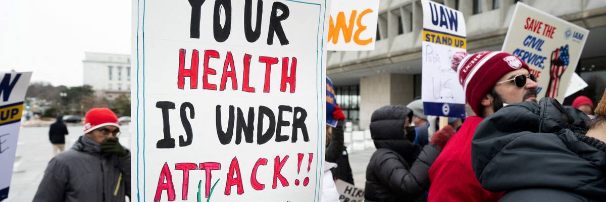 Protester holds sign saying, "Your health is under attack."