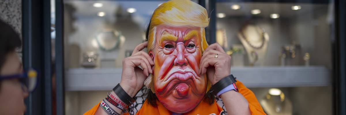 Protester in Trump mask and prison jumpsuit.