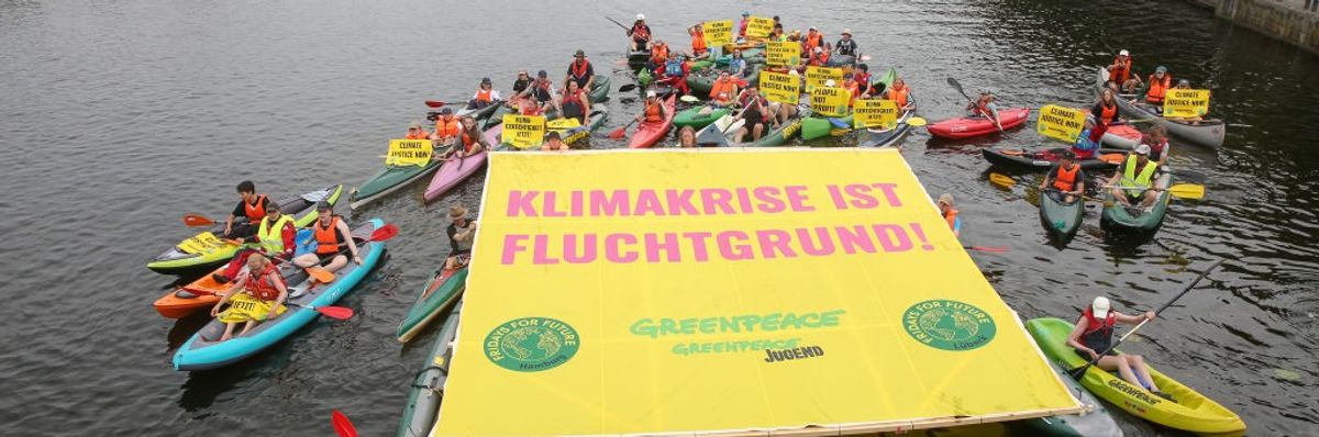 Protesters gather in kayaks holding a yellow sign.