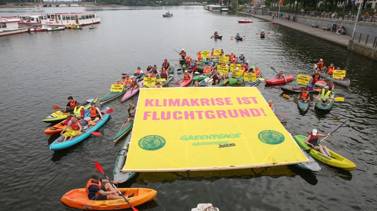 Protesters gather in kayaks holding a yellow sign.