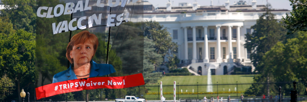 Protesters hoisted a large banner outside the White House calling on German Chancellor Angela Merkel to stop blocking an emergency waiver of intellectual property rules.