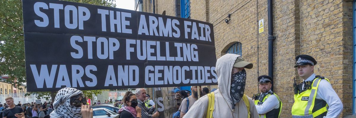 Protesters hold a sign reading "Stop the Arms Fair, Stop Fueling Wars and Genocides"