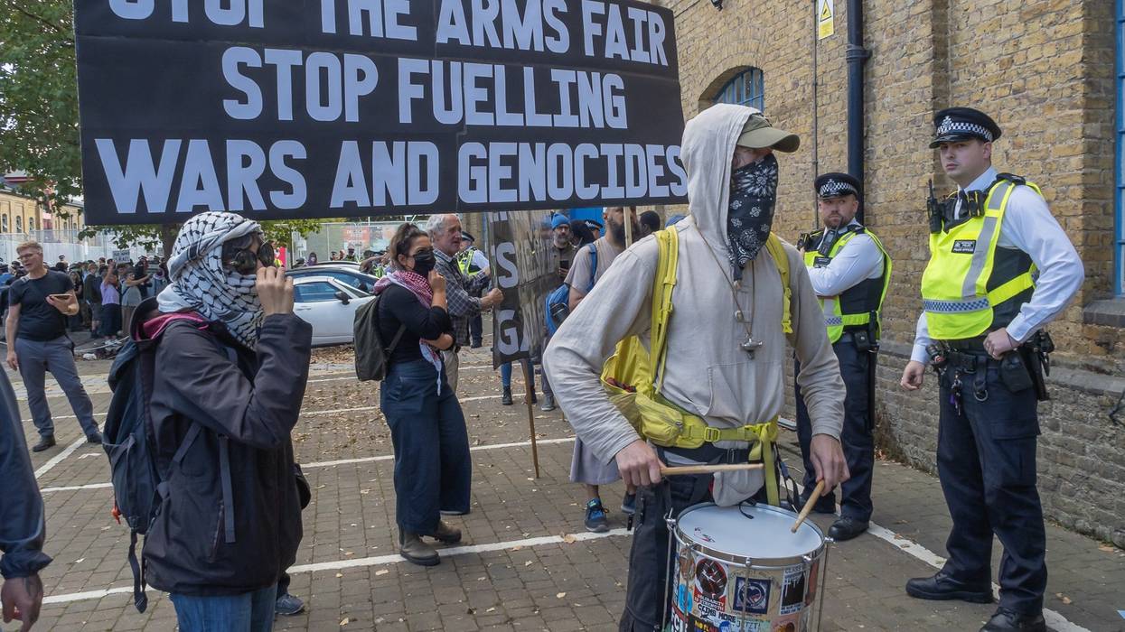 Protesters hold a sign reading "Stop the Arms Fair, Stop Fueling Wars and Genocides"