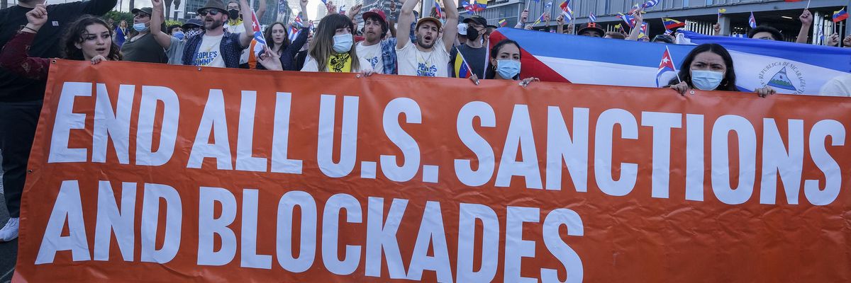 Protesters hold Cuban and Venezuelan flags and a banner reading, "End All U.S. Sanctions and Blockades"